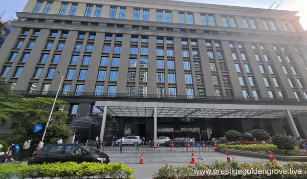 A wide-angle shot of the multi-story AIG corporate building featuring a modern grey facade and glass windows, with a white driveway canopy and cars parked in front, located near the Prestige Golden Grove project.