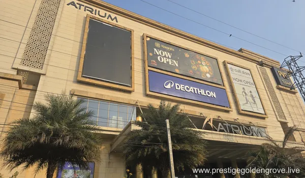 A multi-story modern commercial building with glass facades and white paneling. Visible brand logos include Decathlon and PVR Cinemas. The building is surrounded by paved driveways and minimal greenery under a clear sky.