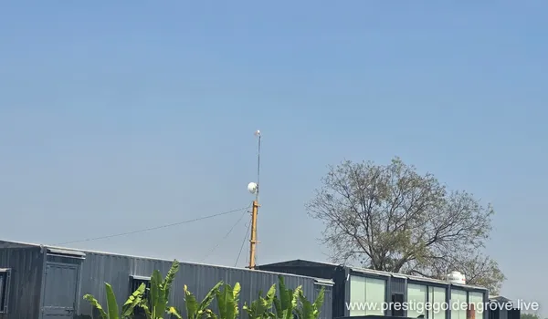A wide paved access road with a black-and-white checkered curb and roadside greenery, showing the transport connectivity near the Prestige Golden Grove development.