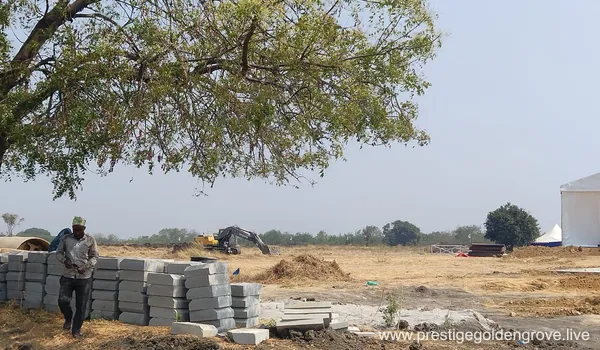 Construction materials and machinery at the Prestige Golden Grove site in Tellapur, Hyderabad, showing initial groundwork and land preparation.